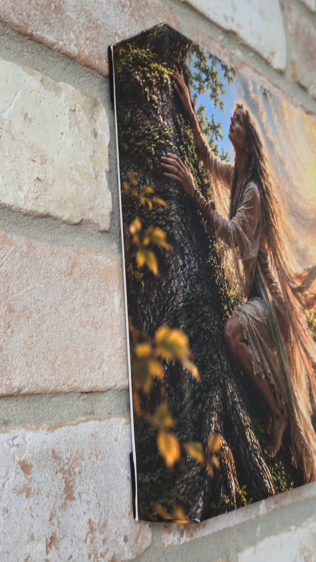A rectangular canvas print or framed artwork lying on a light stone or brick surface. The artwork depicts a fantasy scene with a winged creature or dragon-like figure in warm brown, gold, and dark green tones against a blue sky patch.