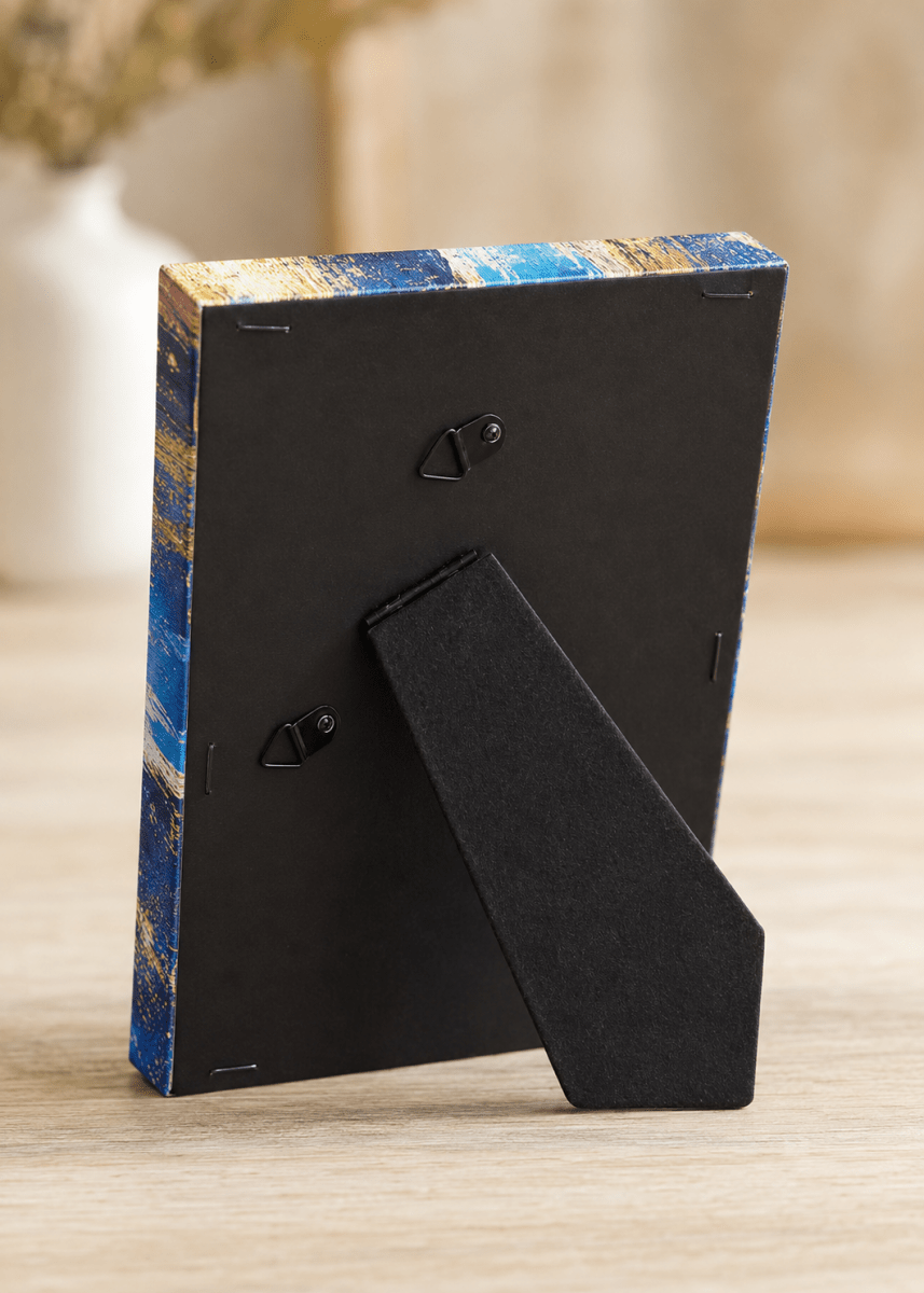 A small rectangular picture frame shown from the back on a light wood surface, with a black backing and a blue-and-gold marbled pattern around the edges.
