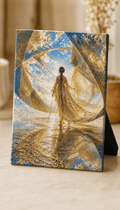 A square canvas art print featuring a woman in a flowing white dress standing in reflective water under a blue sky with large golden translucent shapes, displayed on a tabletop easel black stand.